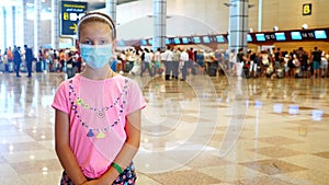 Portrait of child girl in medical protective mask at airport, against background of check-in counters and air passengers