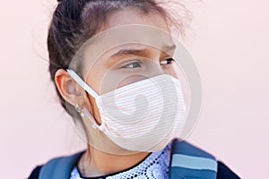 Portrait of child girl ready to school, wearing medical face mask against coronavirus or covid-19. Background of pastel pink color