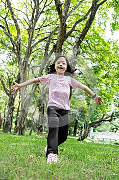 Portrait of child girl running and smiling in green park