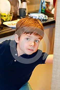 Portrait of child in kitchen. Cute little boy, playing in kitchen. Young kid is hungry, looks at and checks is it finished lunch.