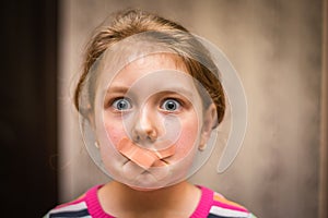 Portrait of a child with a mouth plastered over. The little girl`s mouth was covered with duct tape. A sad, scared child can`t