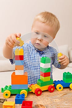 Portrait of child playing with colorful plastic bricks at the table. Toddler having fun and building a train out of constructor