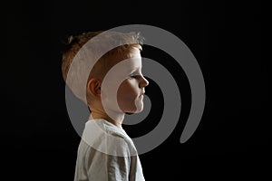 Portrait of a child in profile on a black background. Boy looking forward, concept,