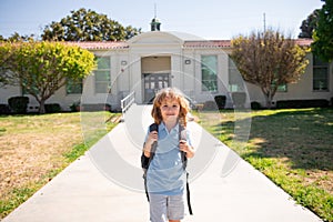 Portrait of child pupul with rucksacks in the park near school. Schoolboy with backpacks outdoors. School building