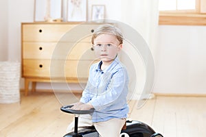 Portrait child riding toy vintage car. Funny kid playing at home. Summer vacation and travel concept. Active little boy driving a