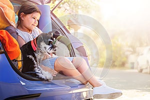 Portrait of a child with a schnauzer dog in the trunk of a car looking