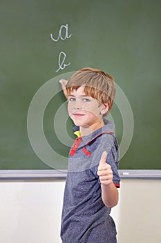 Portrait, child and student with thumbs up on blackboard in classroom, elementary school and mockup. Chalkboard