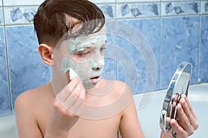 Portrait of child teen boy removing alginate mask from face looking at mirror.