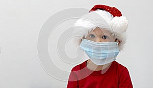 Portrait A child, a toddler in a red santa hat is sick at Christmas. A boy in a medical mask will not go to a matinee in