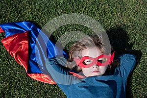 Portrait of child wearing a superhero costume laying on grass. Super hero child having fun in park outdoors. Kids power