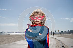 Portrait of child wearing a superhero costume. Super hero child against blue summer sky background. Kid having fun