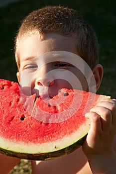 Portrait of a child who eats a watermelon slice on a lawn