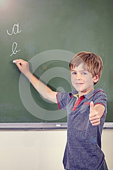 Portrait, child writing and thumbs up on blackboard in classroom, elementary school and mockup. Chalkboard, education