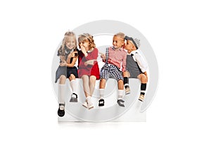 Portrait of children, boys and girls sitting together, whispering, giggling isolated over white studio background