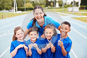 Portrait Of Children With Female Coach Showing Off Winners Medals On Sports Day