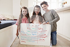 Portrait Of Children Making List Of Chores On Whiteboard At Home