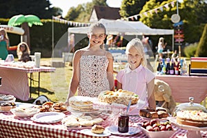 Portrait Of Children Serving On Cake Stall At Busy Summer Garden Fete