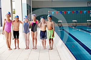 Portrait Of Children Standing On Edge Of Pool Waiting For Swimming Lesson