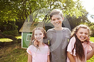 Portrait Of Children Standing In Garden Next To Playhouse