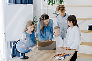 Portrait of children and teacher looking at laptop in the classroom