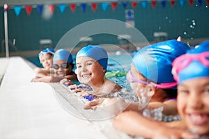 Portrait Of Children In Water At Edge Of Pool Waiting For Swimming Lesson