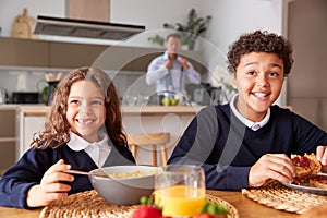 Portrait Of Children Wearing School Uniform Eating Breakfast As Father Gets Ready For Work