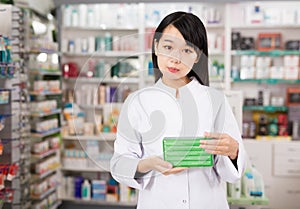 Portrait of chinese female pharmacist is standing with medicines in pharmacy