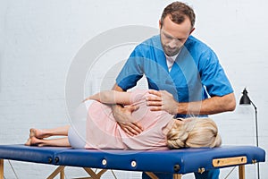 portrait of chiropractor massaging back of patient that lying on massage table