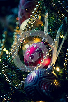 A portrait of christmas ornaments hanging in a christmas tree. It looks like a holiday greeting card with a christmas ball garland