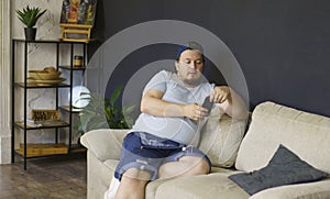 Portrait of chubby casual man sitting at home on sofa and holding smartphone in hands