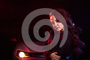 Portrait of chubby teen girl near car illuminated by red light and black background