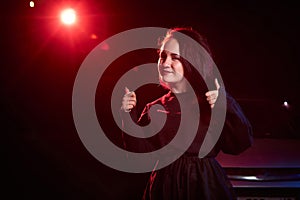 Portrait of chubby teen girl near car illuminated by red light and black background