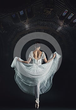 Portrait of the classical ballerina in white dress on black back