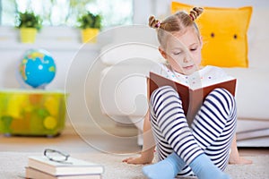 Portrait of clever little girl sitting with book on the floor