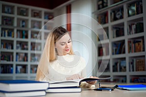 Portrait of clever student with open book reading it in college library.