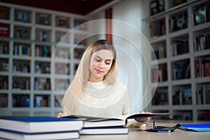 Portrait of clever student with open book reading it in college library.