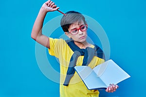 Portrait of a clever and studious boy with red glasses, with a yellow shirt and a sweater on his shoulders, holding a pencil and a