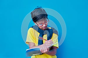 Portrait of a clever and studious boy with red glasses, with a yellow shirt and a sweater on his shoulders, holding a pencil and a