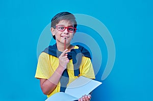 Portrait of a clever and studious boy with red glasses, with a yellow shirt and a sweater on his shoulders, holding a pencil and a