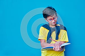 Portrait of a clever and studious boy with red glasses, with a yellow shirt and a sweater on his shoulders, holding a pencil and a