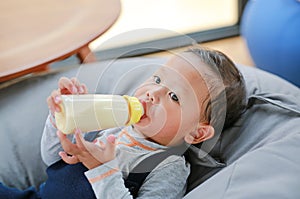 Portrait close up Asian baby boy holding and feeding milk from bottle lying on sofa