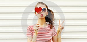 Portrait close up beautiful young woman blowing her lips with red lipstick with red sweet heart shaped lollipop on white