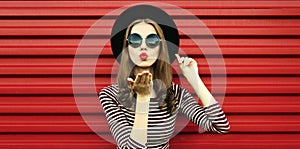 Portrait close up beautiful young woman blowing her red lips sending air kiss wearing a black round hat on a background