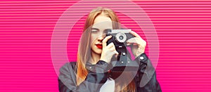 Portrait close up of blonde young woman photographer taking picture with film camera on pink background