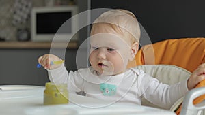 Portrait. Close-up. Cheerful child takes a spoon from his mother and tries to eat. Baby in a feeding chair