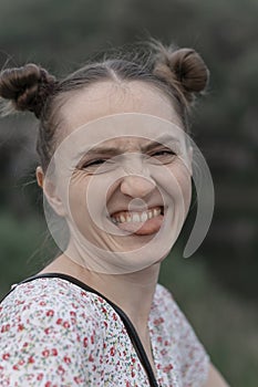 Portrait close up of cheerful young woman with two ponytails showing her tongue to camera and wrinkling her nose