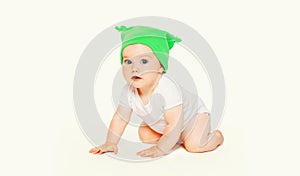 Portrait close up of cute baby crawling on the floor wearing green winter knitted hat on white background