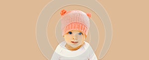 Portrait close up of cute smiling baby in pink knitted hat with bear ears on beige studio background