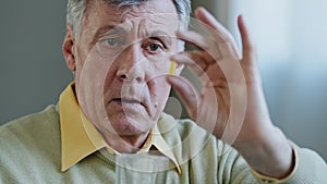 Portrait close-up of elderly man holding pill sad grandfather look at capsule serious mature old pensioner show medical