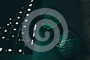 Portrait and close up of glasses on laptop with the light of screen with green binary numbers